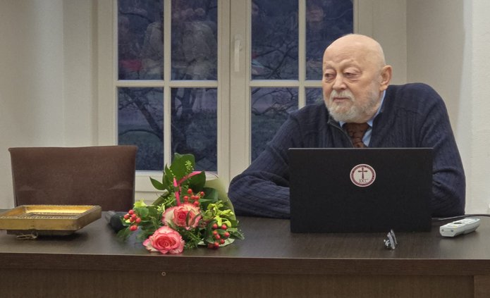 Prof. ALeksander Naumow za stołem, obok leży bukiet kwiatów